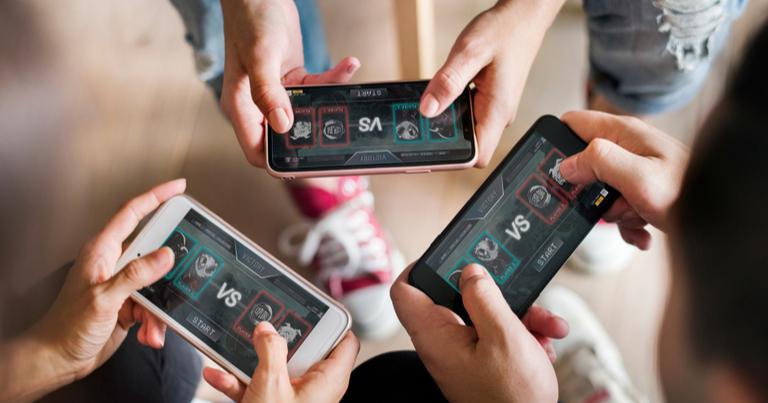 Primer plano de tres personas jugando a un juego online con sus teléfonos móviles.