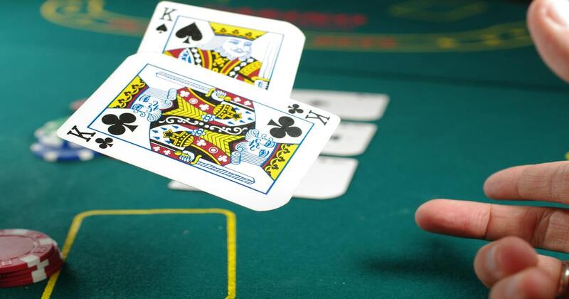 Dos cartas lanzadas por una mano en el aire sobre un tapete de blackjack.