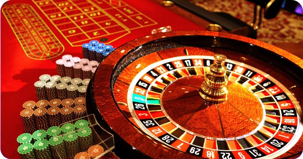 Ruleta de casino sobre mesa roja con fichas apiladas.