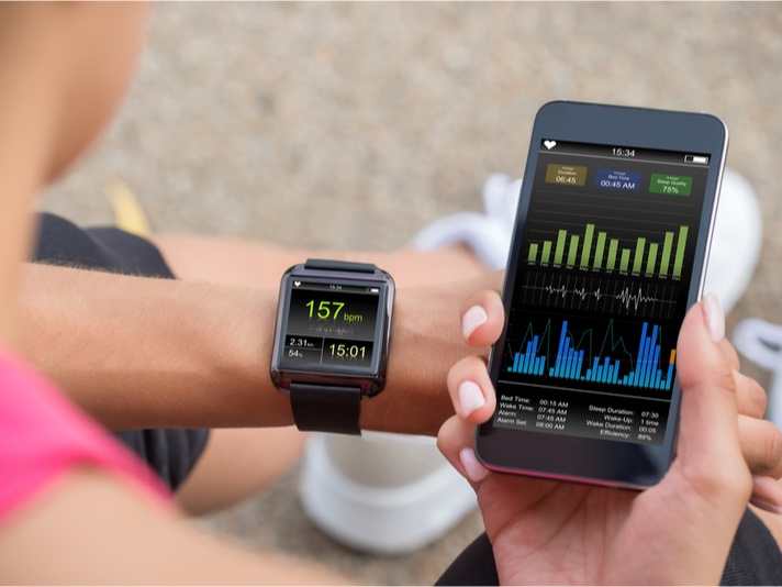 Una mujer mira su reloj fitness y la aplicación correspondiente en su teléfono móvil mientras hace ejercicio.