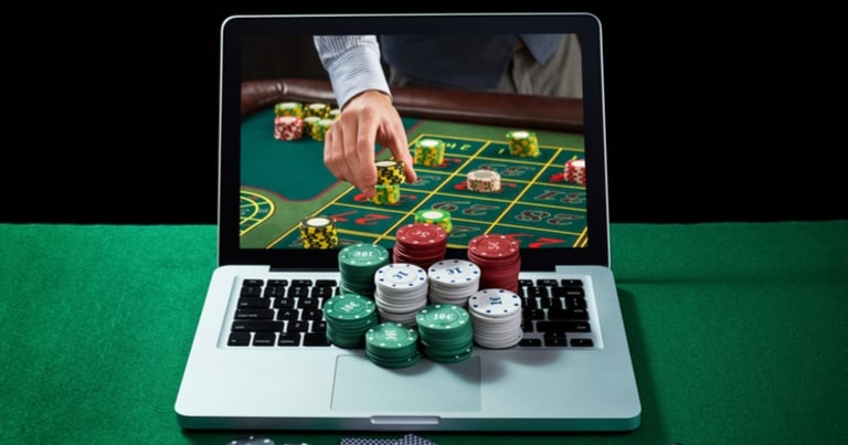  Un ordenador portátil con un crupier colocando fichas en vivo en la pantalla y fichas de casino en el teclado.
