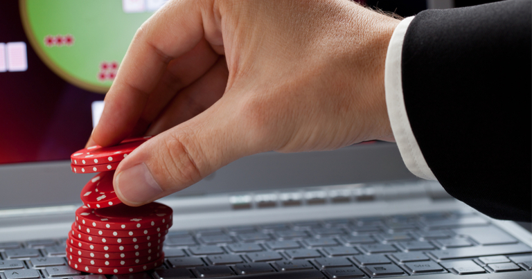 Persona sosteniendo fichas de póquer rojas apiladas sobre el teclado de un ordenador portátil