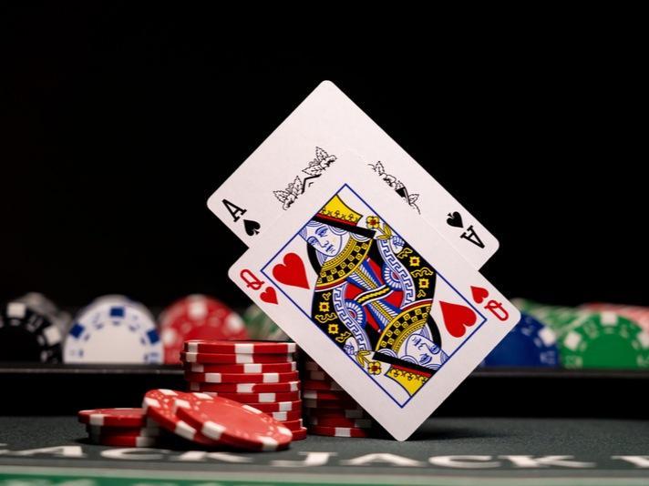 Mesa de casino con fichas y dos cartas suspendidas en el aire que suman un blackjack.