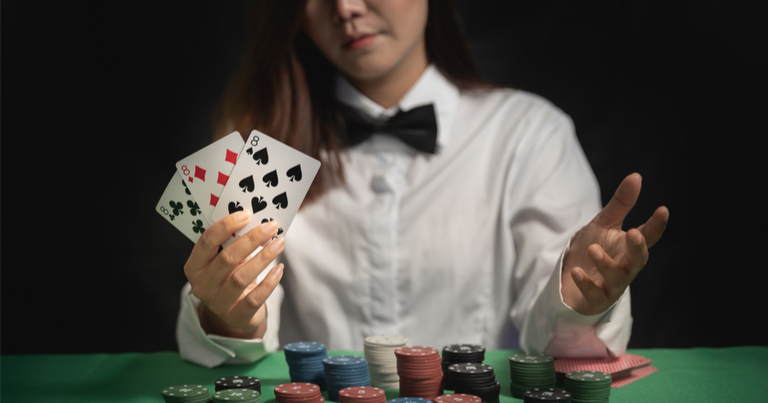 Distribuidor o croupier baraja tarjetas de poker en un casino al fondo de una mesa.