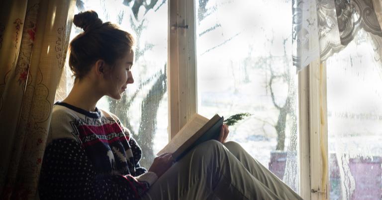 Mujer sentada en el alféizar de una ventana, leyendo un libro