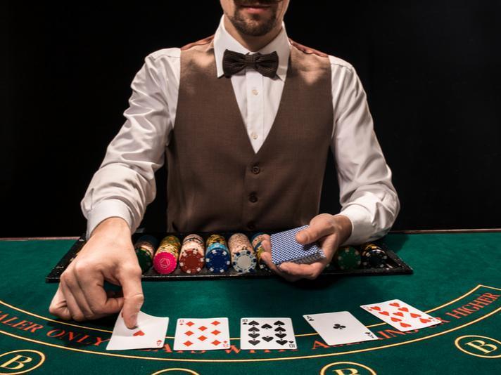 Un crupier de póquer con fichas delante de él y repartiendo cartas en una mesa de juego.