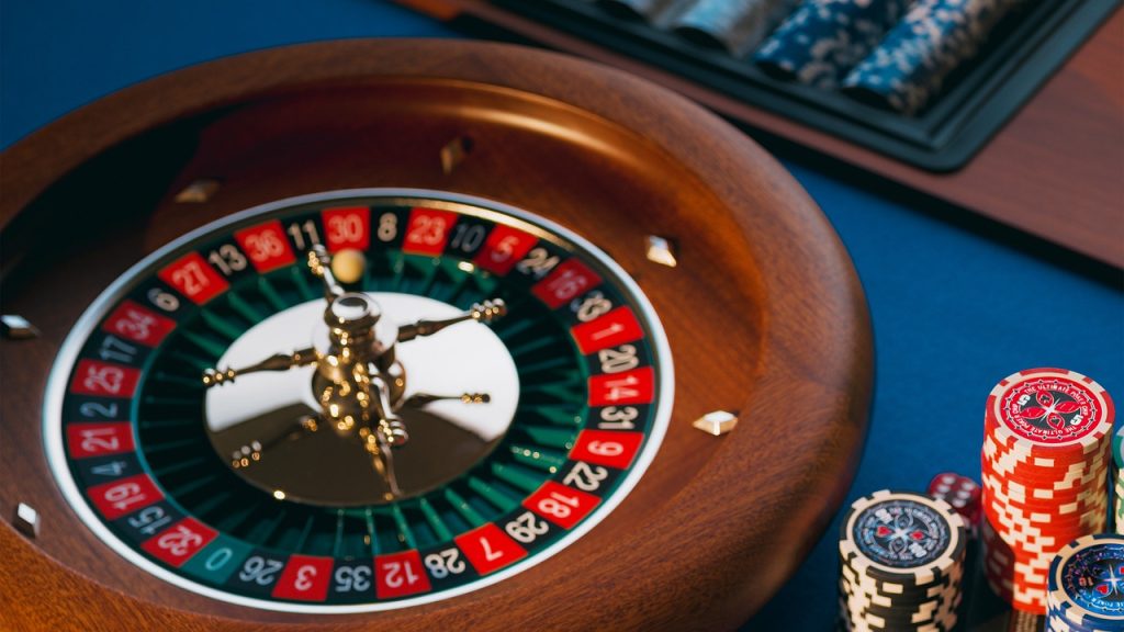 Roda roulette dengan beberapa tumpukan tumpukan chip di atas kain kasa biru.